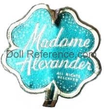 Alexander doll label four leaf clover in metallic turquoise and silver with company name.